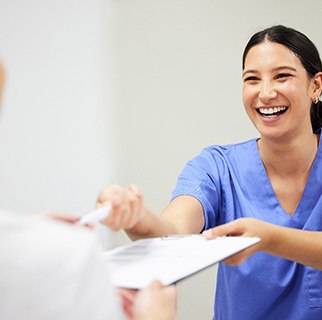 Smiling dental assistant handing patient forms
