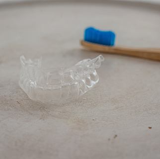 Clear aligners next to wooden toothbrush with blue bristles on textured surface
