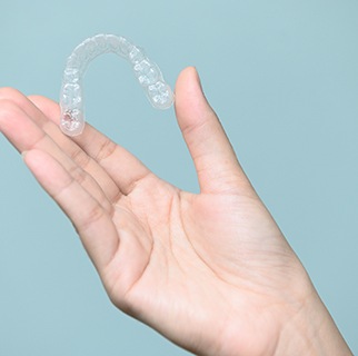 Hand holding a single Invisalign tray with seafoam background